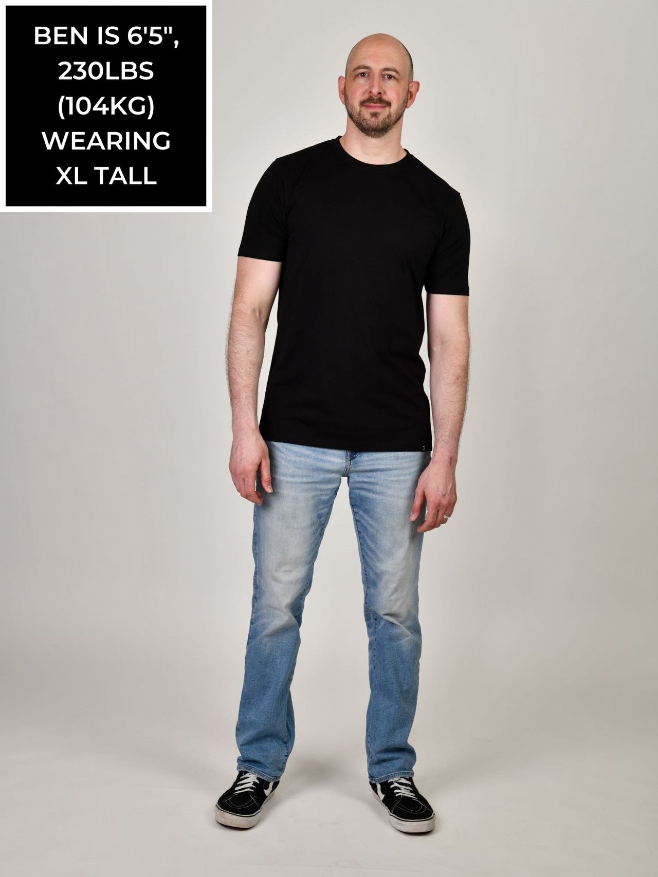 A head to toe shot of a tall and slim guy in the studio wearing a black XL tall slim t-shirt.