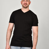 A tall and slim guy smiling in the studio and wearing a black XL tall slim v-neck t-shirt.