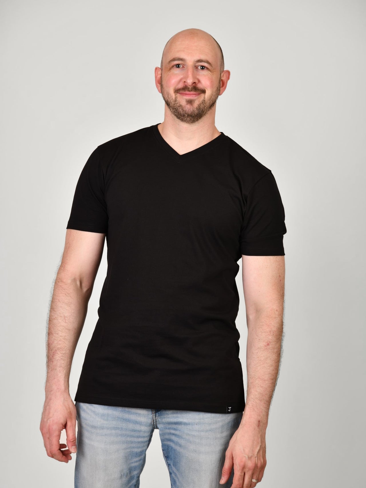 A tall and slim guy smiling in the studio and wearing a black XL tall slim v-neck t-shirt.