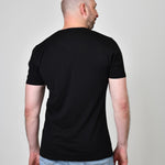 A shot from behind of a tall and slim guy in the studio and wearing a black XL tall slim v-neck t-shirt.