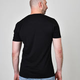 A shot from behind of a tall and slim guy in the studio and wearing a black XL tall slim v-neck t-shirt.