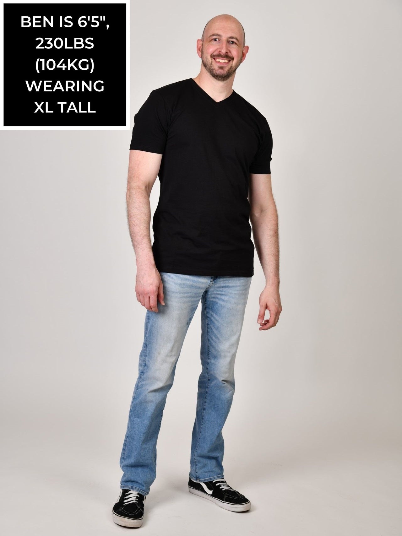 A head to toe shot of a tall and slim guy in the studio wearing a black XL tall slim v-neck t-shirt.