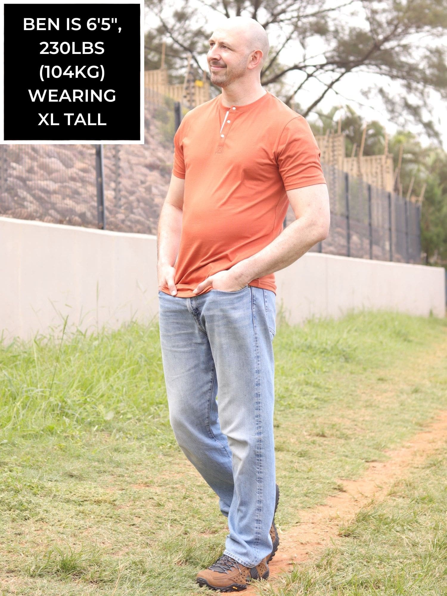 A head to toe shot of a tall skinny guy wearing a tall brown henley shirt.