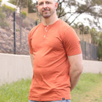 A tall slim guy, hands behind back, wearing a brown XL tall henley shirt.