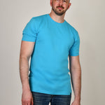 A tall and slim guy smiling in the studio and wearing a cyan XL tall slim t-shirt.