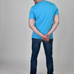 A shot from behind of a tall and slim guy in the studio and wearing a cyan XL tall slim t-shirt.