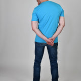 A shot from behind of a tall and slim guy in the studio and wearing a cyan XL tall slim t-shirt.