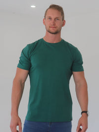 Thumbnail for A tall and broad guy smiling in the studio and wearing a dark green 2XL tall slim t-shirt.