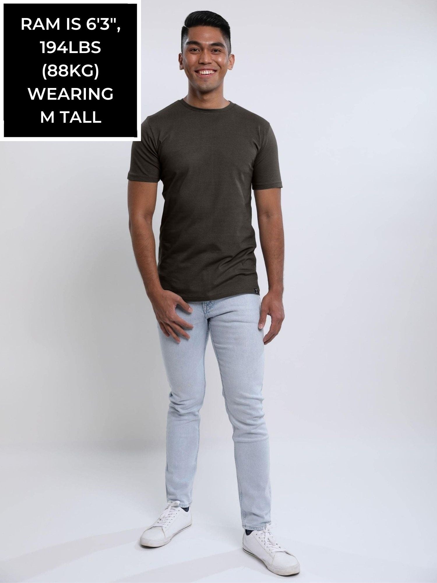 A head to toe shot of a tall and slim guy in the studio wearing a grey medium tall slim t-shirt.