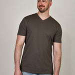 A tall and slim guy smiling in the studio and wearing a dark grey XL tall slim v-neck t-shirt.