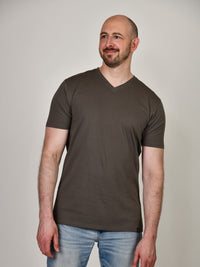 Thumbnail for A tall and slim guy smiling in the studio and wearing a dark grey XL tall slim v-neck t-shirt.