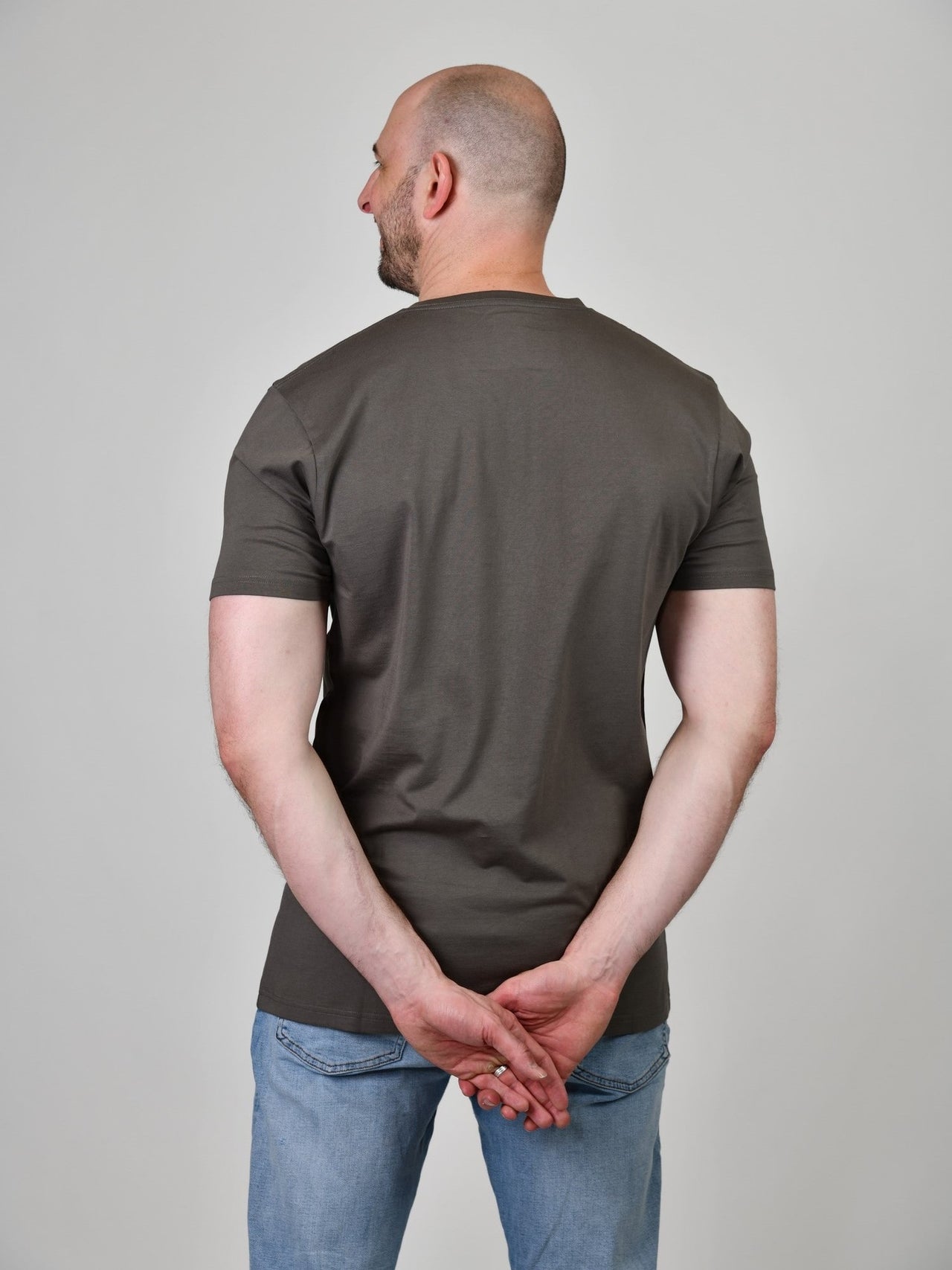 A shot from behind of a tall and slim guy in the studio and wearing a dark grey XL tall slim v-neck t-shirt.