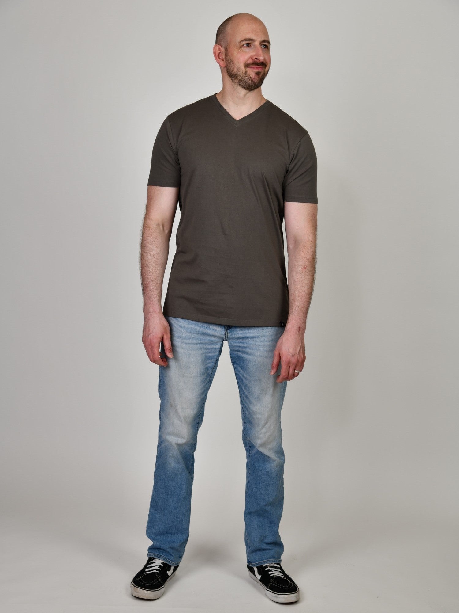 A head to toe shot of a tall and slim guy in the studio wearing a dark grey XL tall slim v-neck t-shirt.