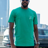 A tall and skinny guy in the street and wearing a green minimal graphic tall t-shirt.