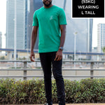 A head to toe shot of a tall and skinny guy in the street and wearing a green minimal graphic tall t-shirt.