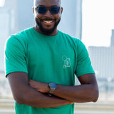 A tall and skinny guy in the street, arms folded, and wearing a green minimal graphic tall t-shirt.