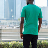 A shot from behind of a tall skinny guy in the street and wearing a green tall slim fit t-shirt.