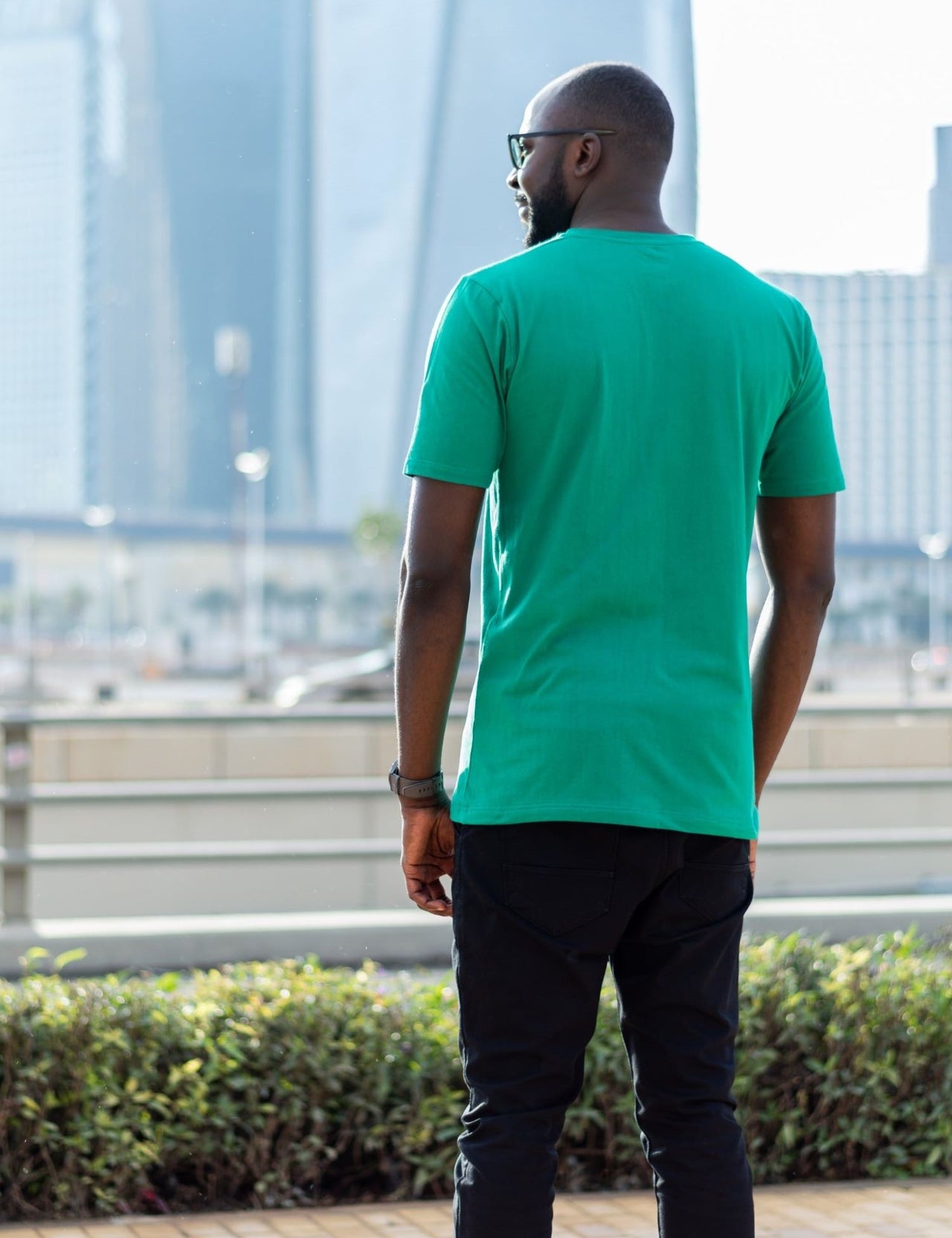 A shot from behind of a tall skinny guy in the street and wearing a green tall slim fit t-shirt.