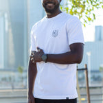 A tall and skinny guy in the street and wearing a white minimal graphic tall t-shirt.