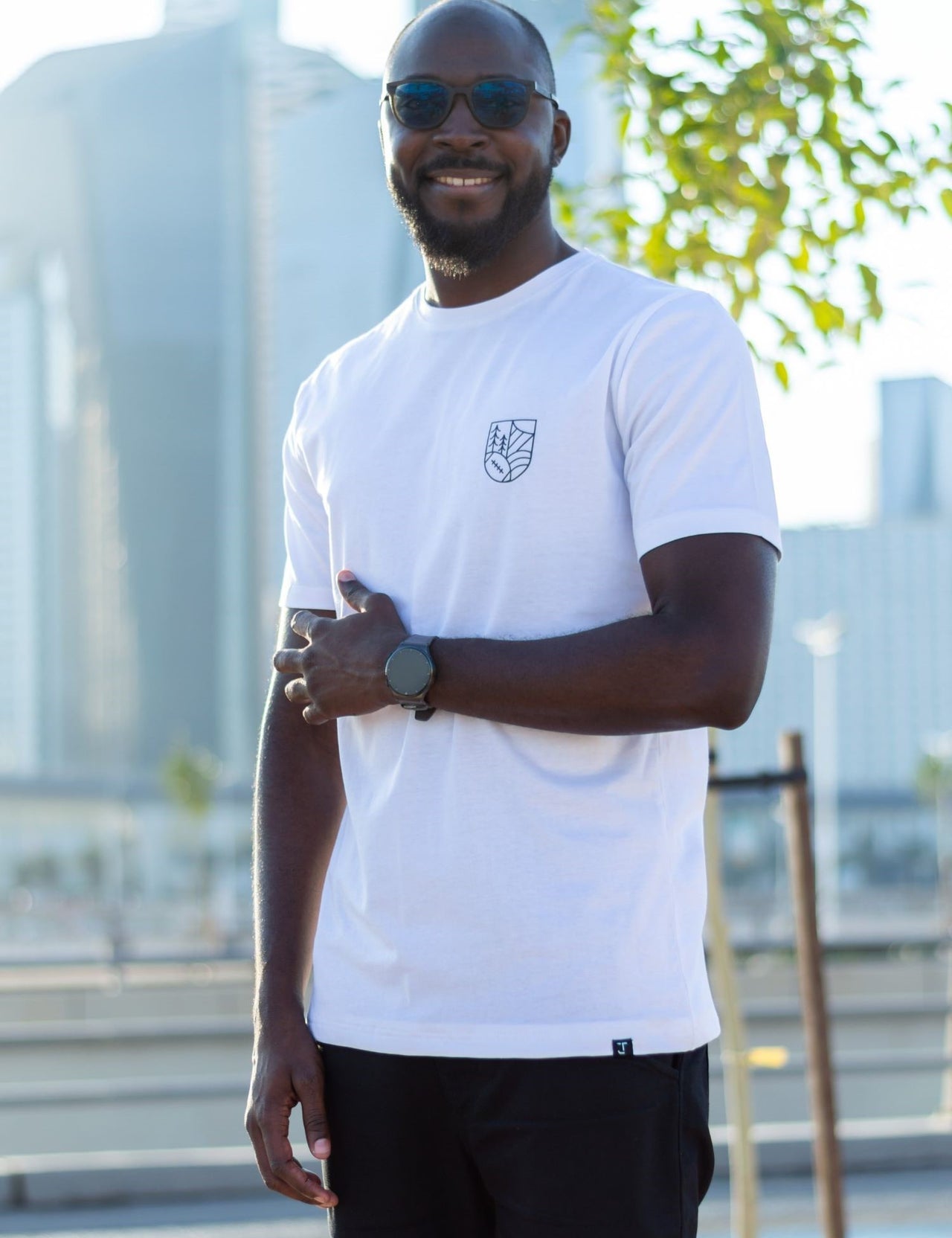 A tall and skinny guy in the street and wearing a white minimal graphic tall t-shirt.