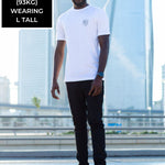 A head to toe shot of a tall and skinny guy in the street and wearing a white minimal graphic tall t-shirt.