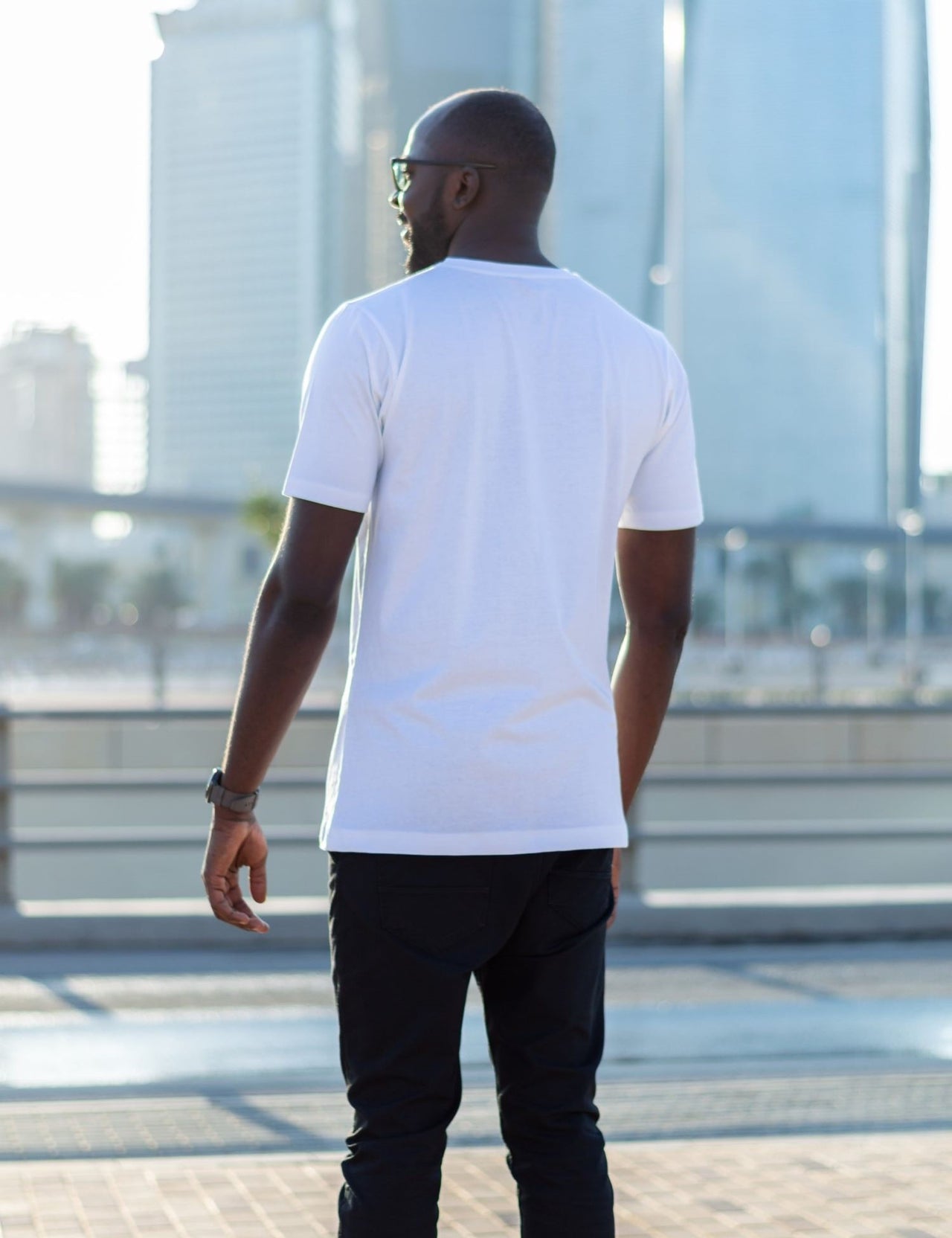 A shot from behind of a tall skinny guy in the street and wearing a white tall slim fit t-shirt.