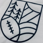 A close up shot of the graphic on the upper left chest of the t-shirt: a volleyball, a tree, hills and the Sun shaped into a crest.