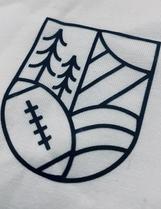 A close up shot of the graphic on the upper left chest of the t-shirt: a volleyball, a tree, hills and the Sun shaped into a crest.
