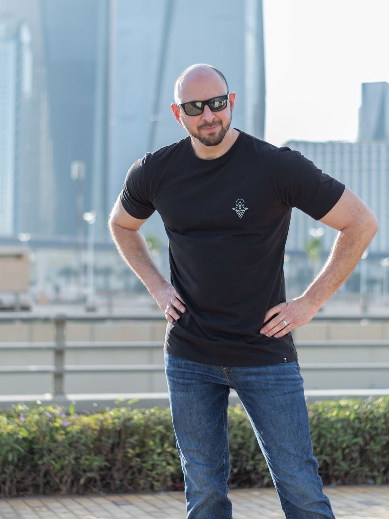 A tall and slim guy in the street with his hands on his hips and wearing a black minimal graphic tall t-shirt.