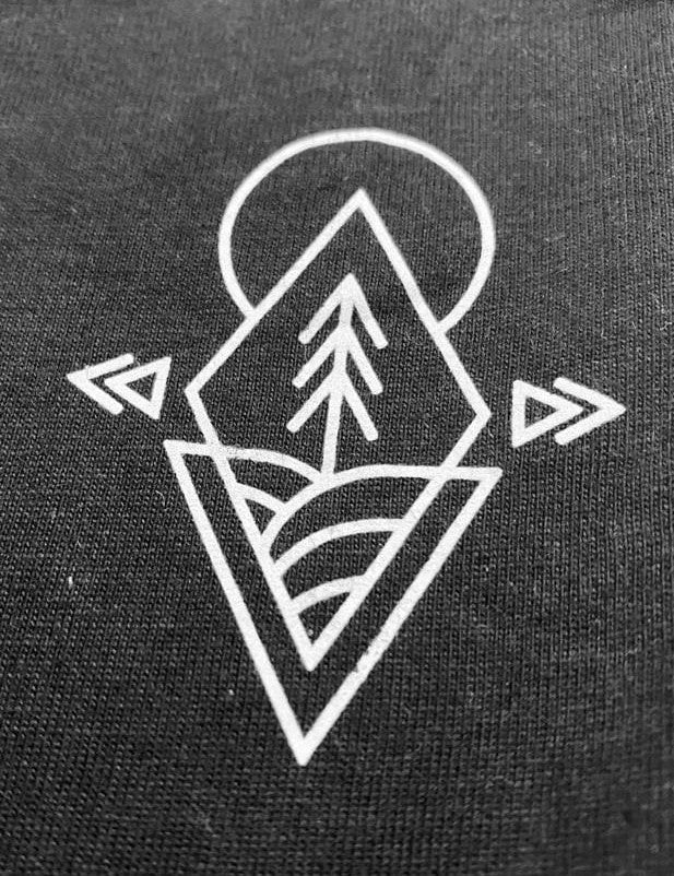 A close up shot of the graphic on the upper left chest of the t-shirt: a tree, hills and the Sun shaped into a diamond.