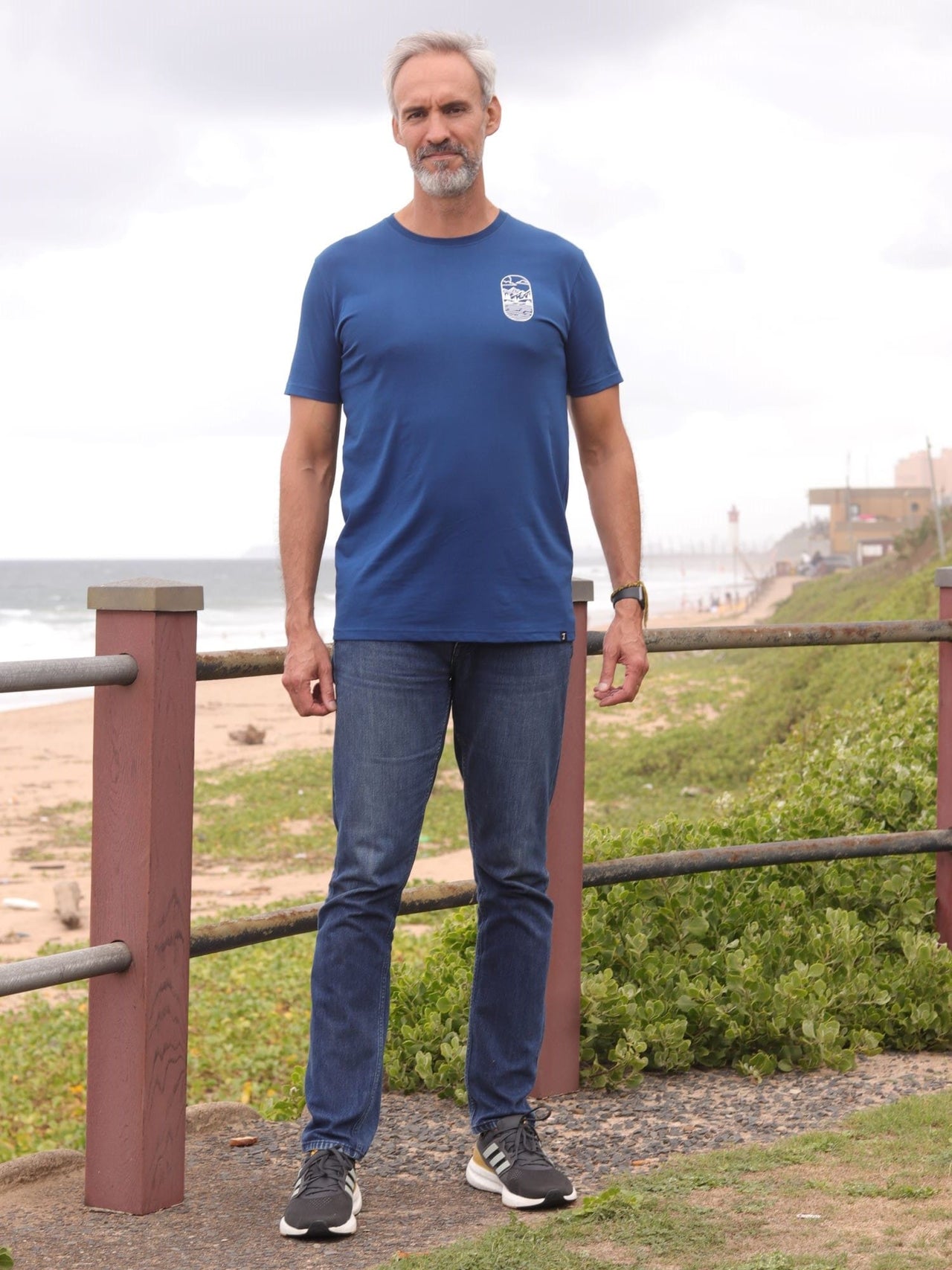 A head to toe shot of a tall slim guy in an L tall graphic t-shirt with a lake design.