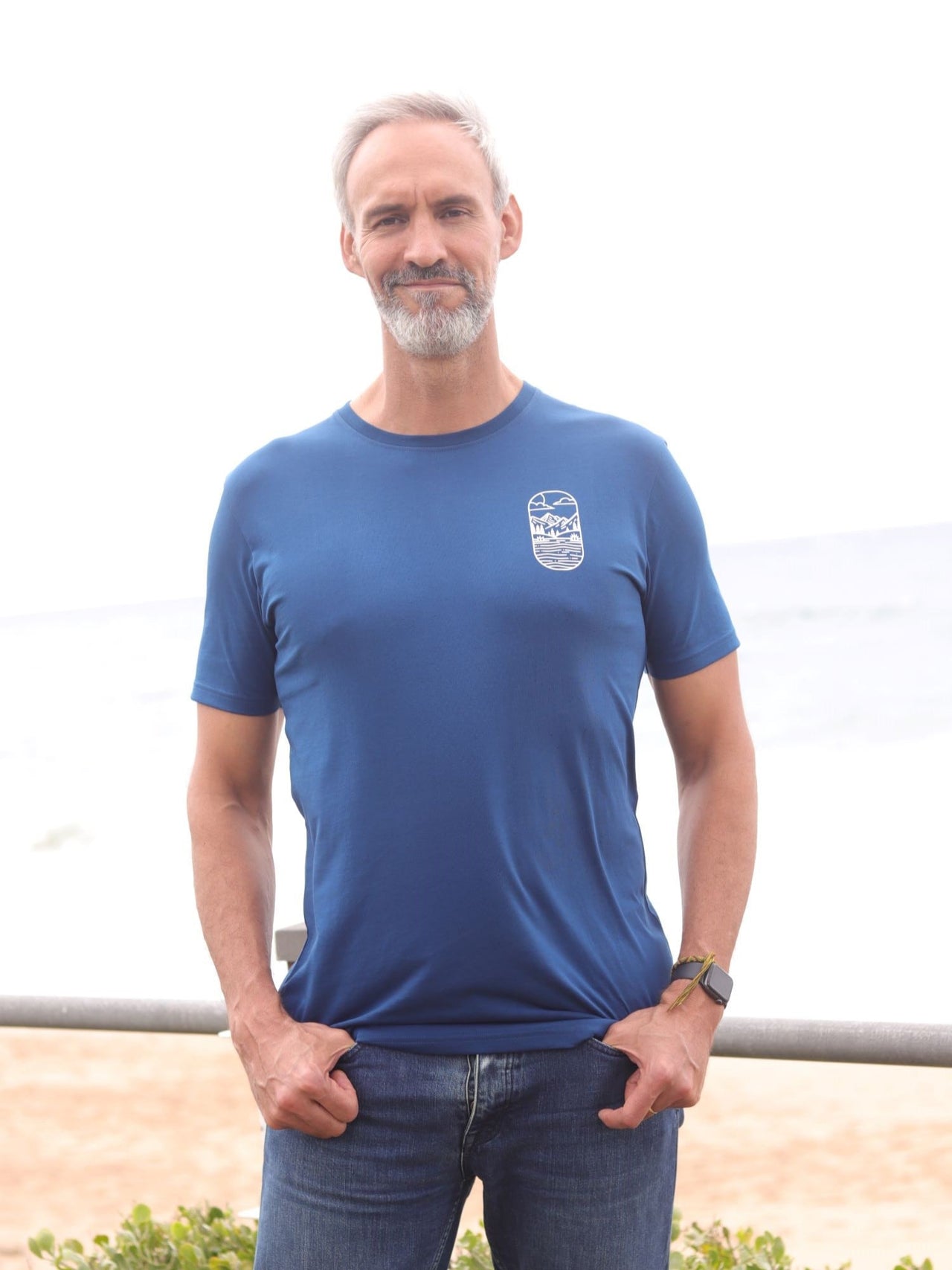 An upper body shot of a tall slim guy in an L tall graphic t-shirt with a lake design, hands in pockets.