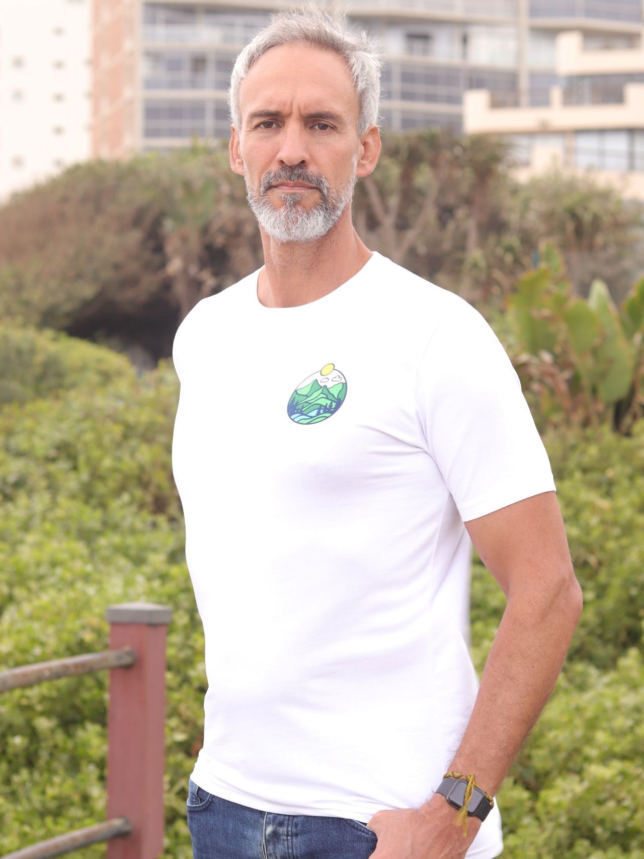 An upper body shot of a tall slim guy in an L tall graphic t-shirt with a landscape design, hands in pockets.