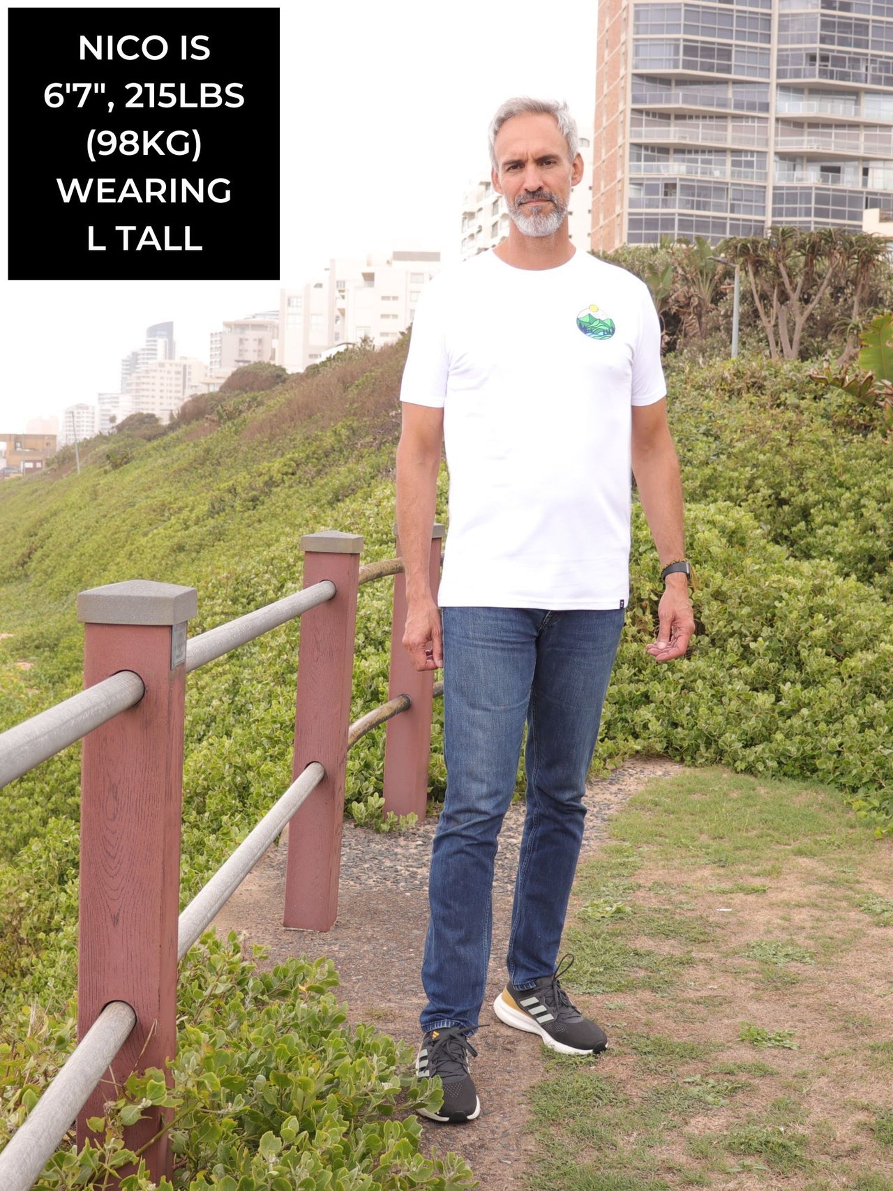 A head to toe shot of a tall slim guy in an L tall graphic t-shirt with a landscape design.