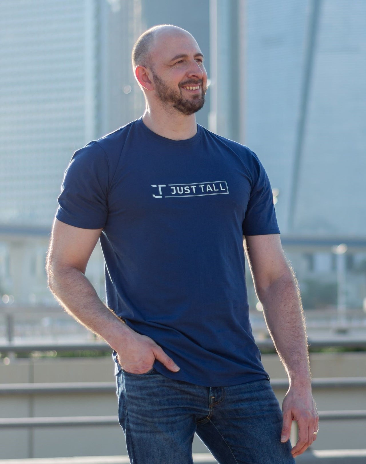 A tall and slim guy in the street, one hand in his pocket and wearing a navy blue Just Tall branded tall t-shirt.