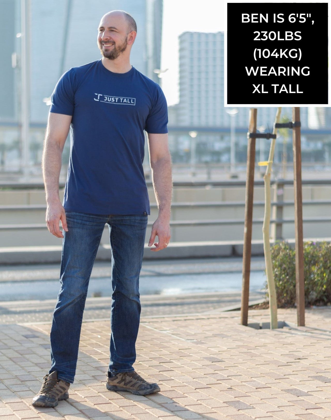A head to toe shot of a tall and slim guy in the street and wearing a navy blue Just Tall branded graphic tall t-shirt.