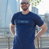 A tall and slim guy in the street with his hands behind his back and wearing a navy blue Just Tall branded graphic tall t-shirt.
