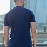 A shot from behind of a tall slim guy in the street and wearing a navy blue tall slim fit t-shirt.