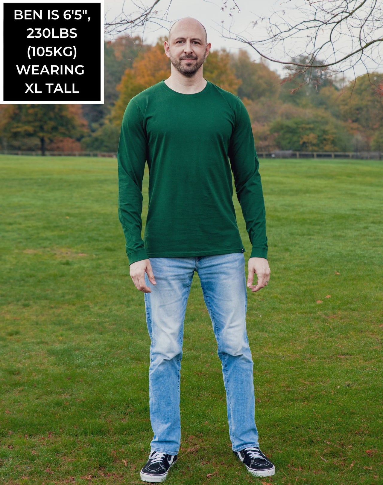 A head to toe shot of a tall athletic guy in a park wearing a dark green long sleeve tall t-shirt.