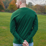 A shot from behind of a tall athletic guy wearing a long sleeve dark green tall t-shirt, hands crossed behind his back.