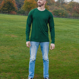 A head to toe shot of a tall athletic guy in a park, looking up at the sky and wearing a dark green long sleeve tall t-shirt.