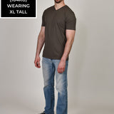 A head to toe shot of a tall and slim guy in the studio wearing a dark grey XL tall slim v-neck t-shirt.