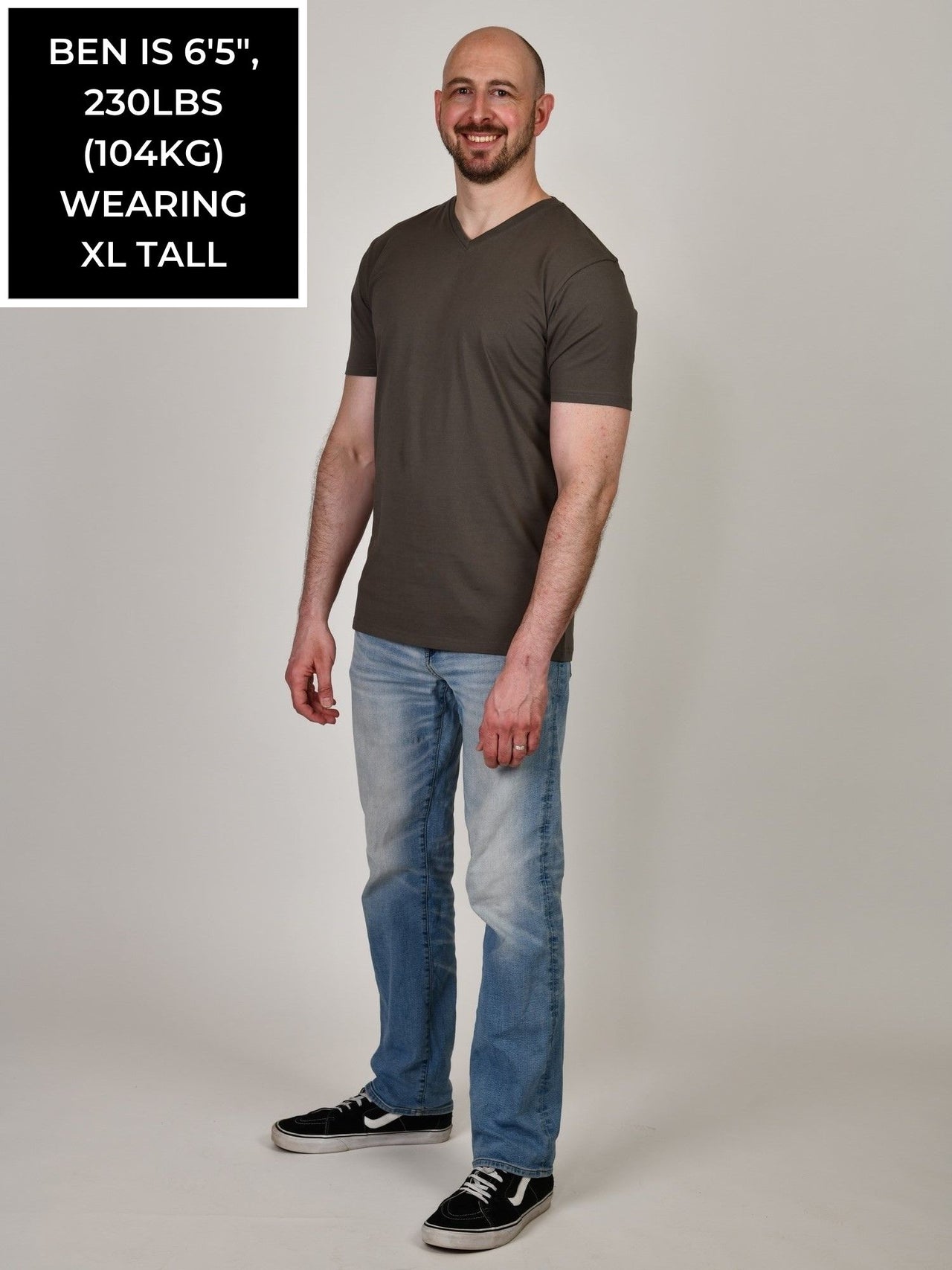 A head to toe shot of a tall and slim guy in the studio wearing a dark grey XL tall slim v-neck t-shirt.
