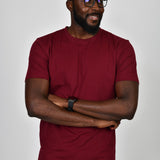 A tall and slim guy smiling in the studio, hands folded and wearing a cabernet L tall slim t-shirt.