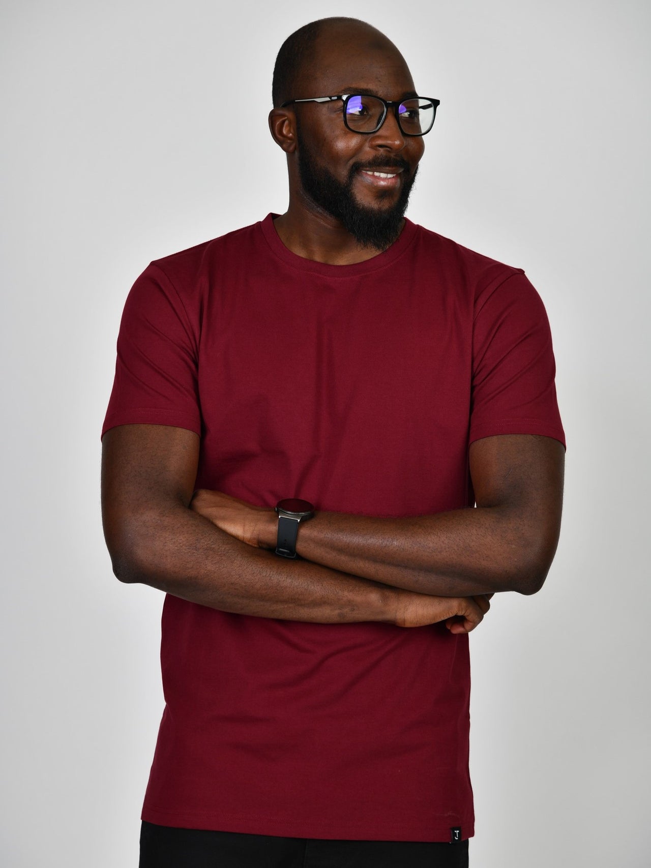 A tall and slim guy smiling in the studio, hands folded and wearing a cabernet L tall slim t-shirt.