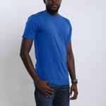 A tall and athletic guy in the studio with one hand in pocket wearing a blue large tall slim t-shirt.