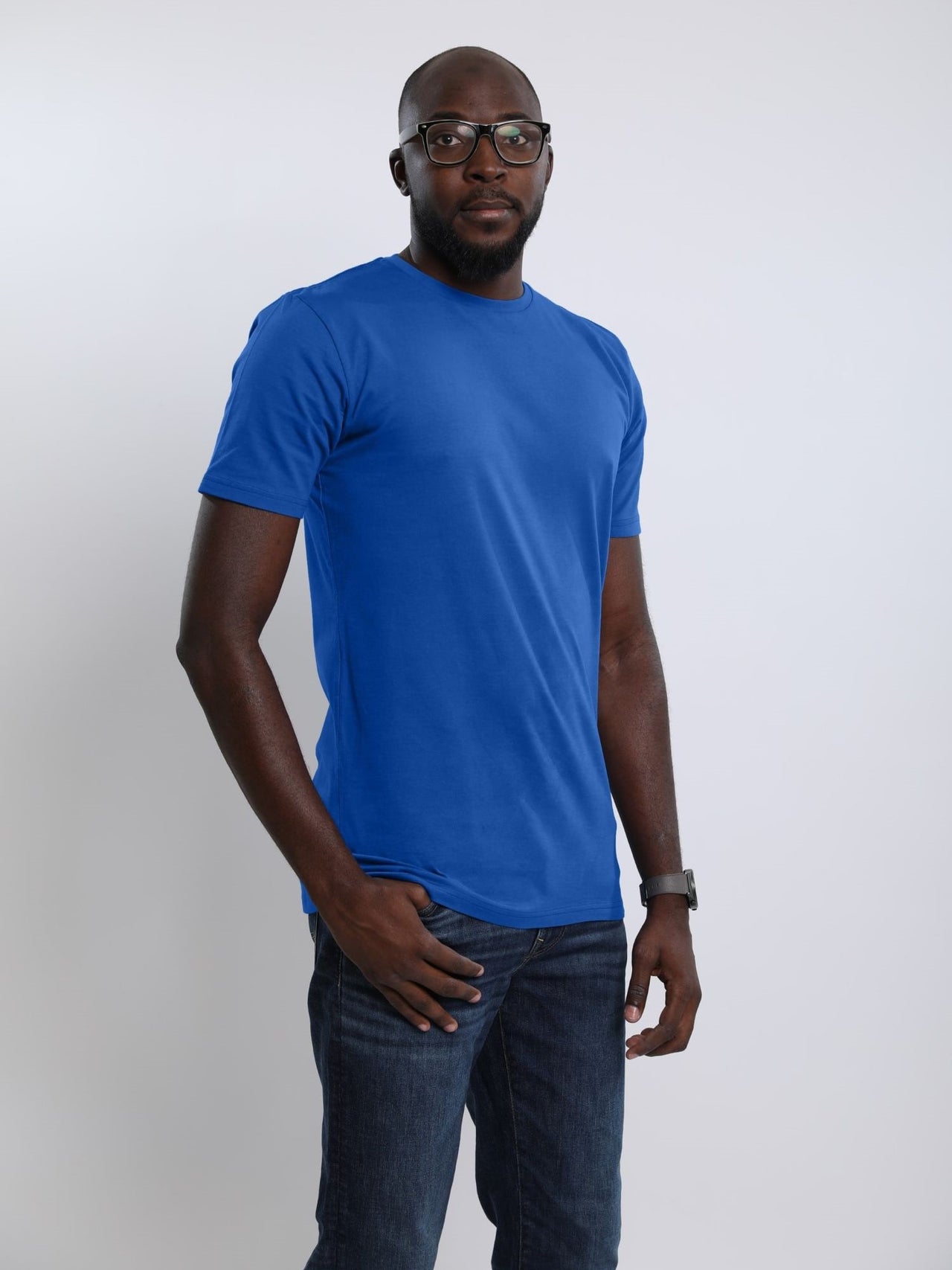A tall and athletic guy in the studio with one hand in pocket wearing a blue large tall slim t-shirt.