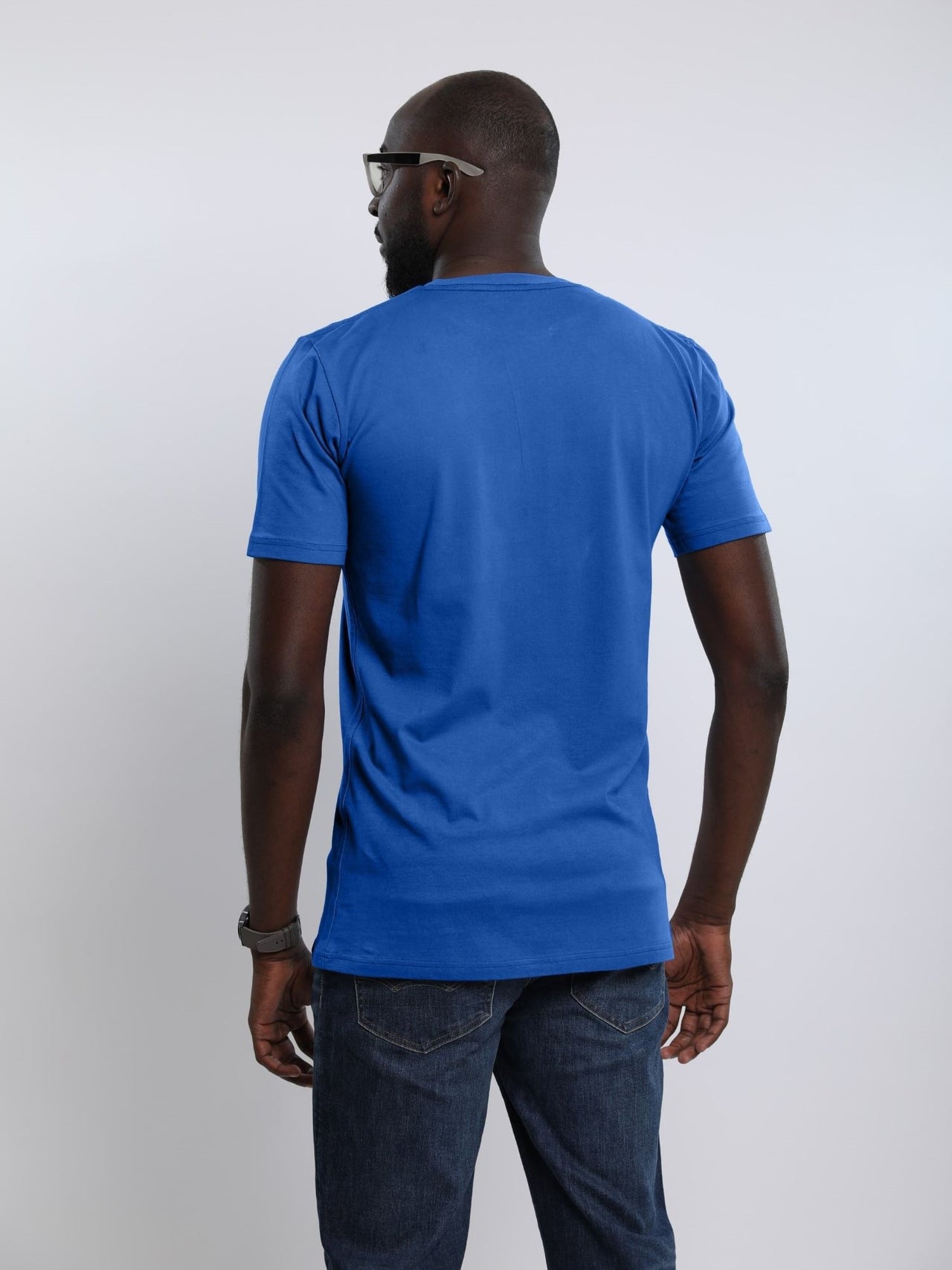 A shot from behind of a tall and athletic guy in the studio wearing a blue large tall slim t-shirt.