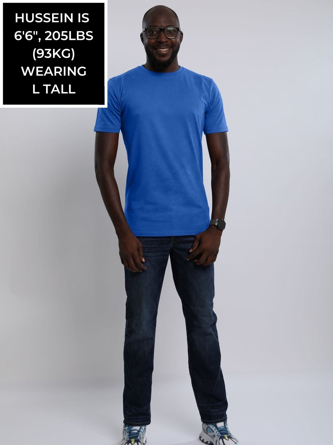 A head to toe shot of a tall and athletic guy in the studio wearing a blue large tall slim t-shirt.