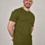 A shot of a tall athletic guy, hands behind back, wearing a military green XL tall t-shirt.